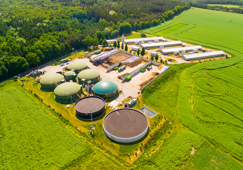 Aerial view over biogas plant and farm in green fields