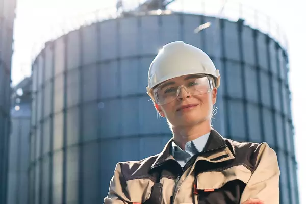 female worker in helmet standing in front of big tanks